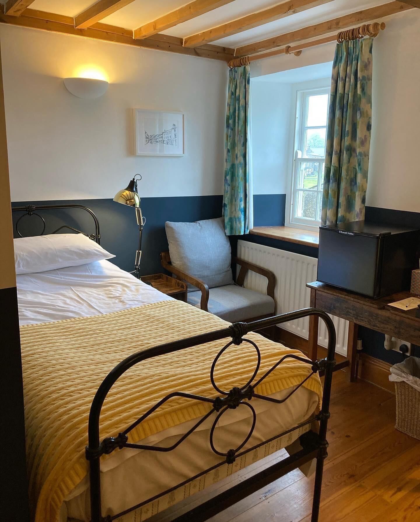 A bedroom with a bed, a chair, a desk with a computer, and a window with curtains.