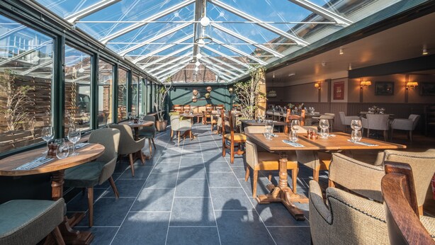 A restaurant with a glass ceiling, wooden tables, and chairs.