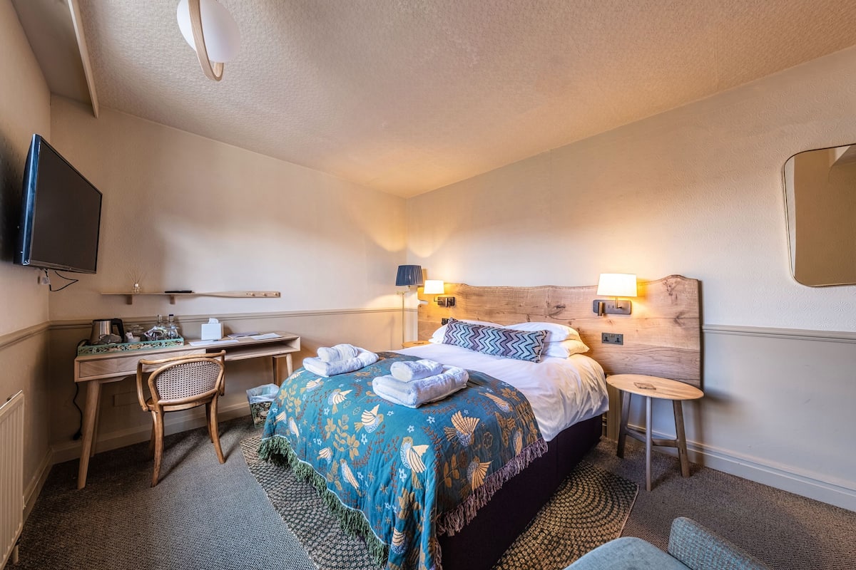 A hotel room with a bed, a desk, a chair, a television, and a small table.