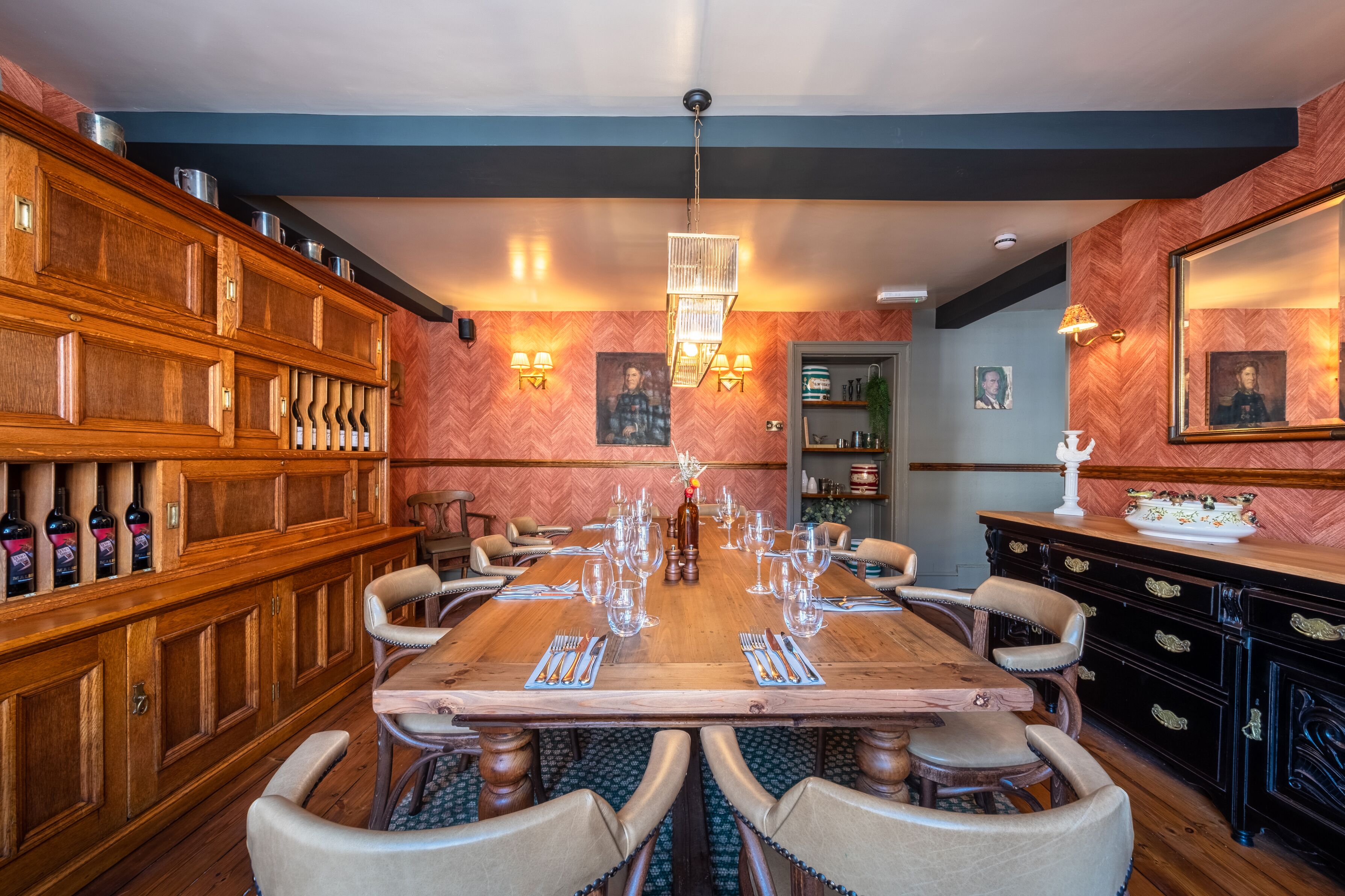 A dining area with a wooden table set for six, flanked by a wine rack and a cabinet with drawers.