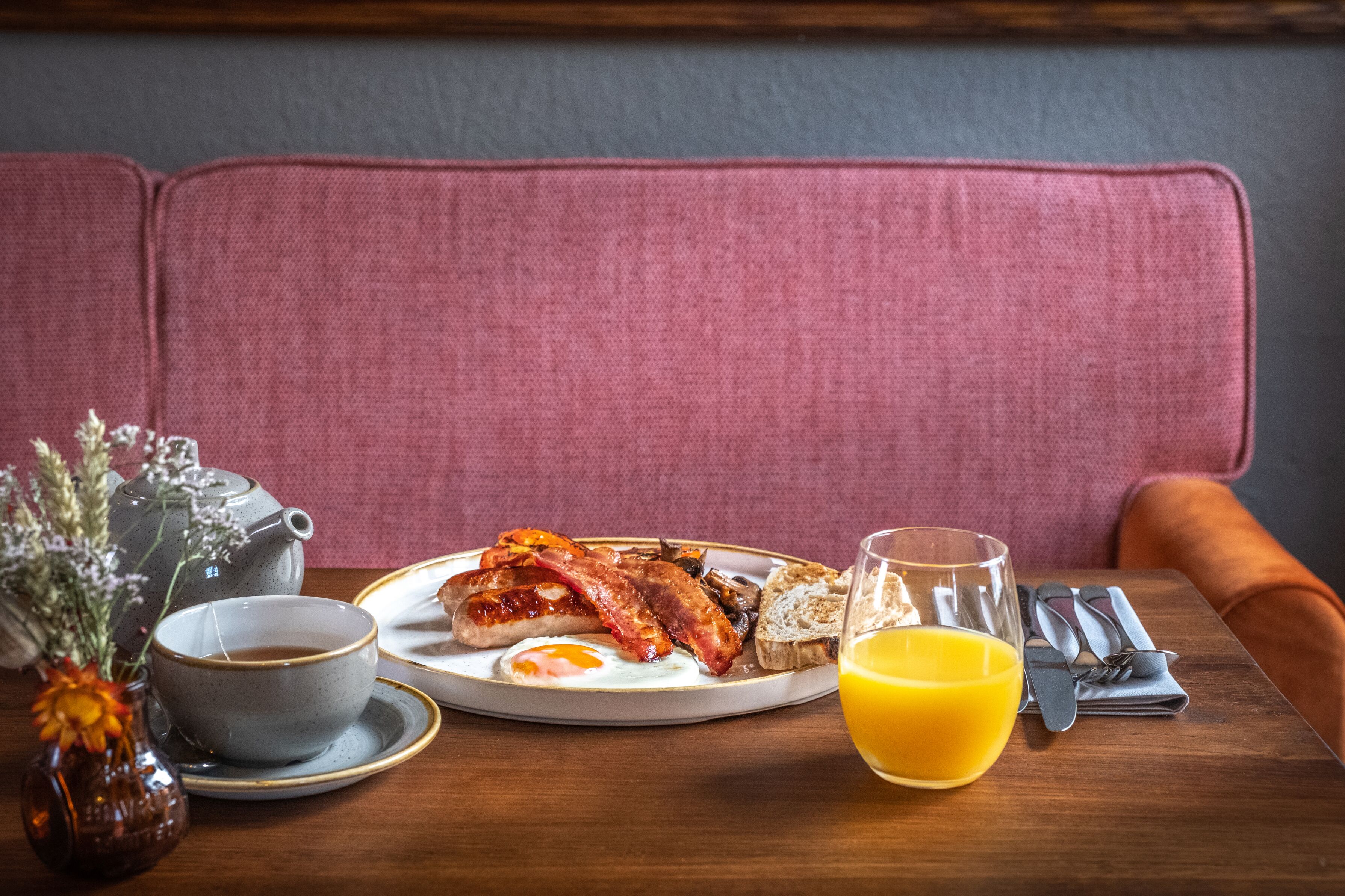 A breakfast setting with a plate of eggs, bacon, toast, and a glass of orange juice on a wooden table.