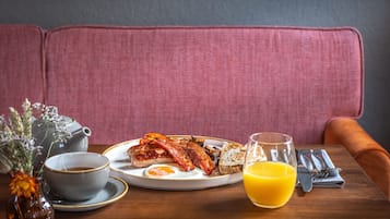 A breakfast setting with a plate of eggs, bacon, toast, and a glass of orange juice on a wooden table.