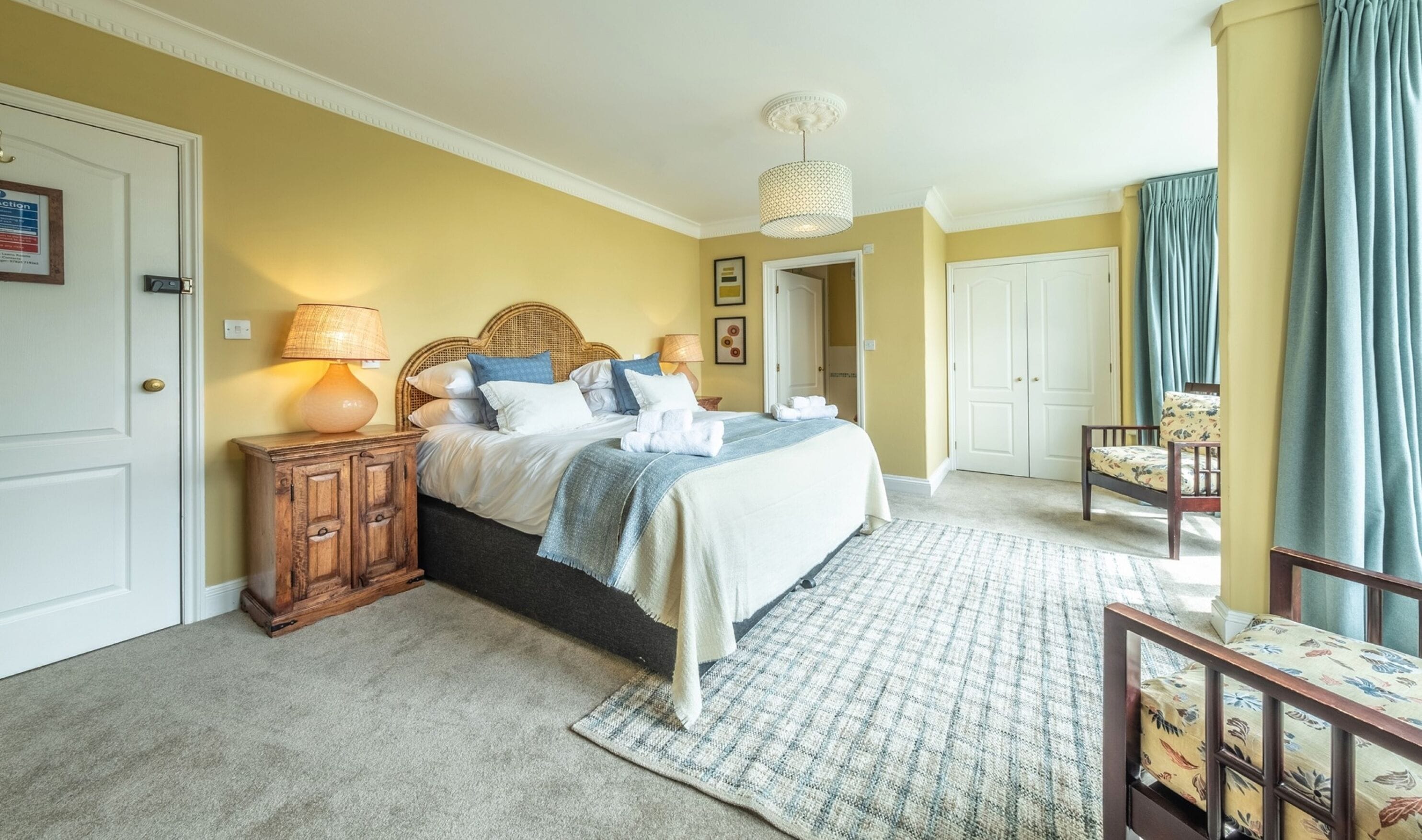 Un dormitorio con cama, mesitas de noche, una lámpara, una silla y una puerta.