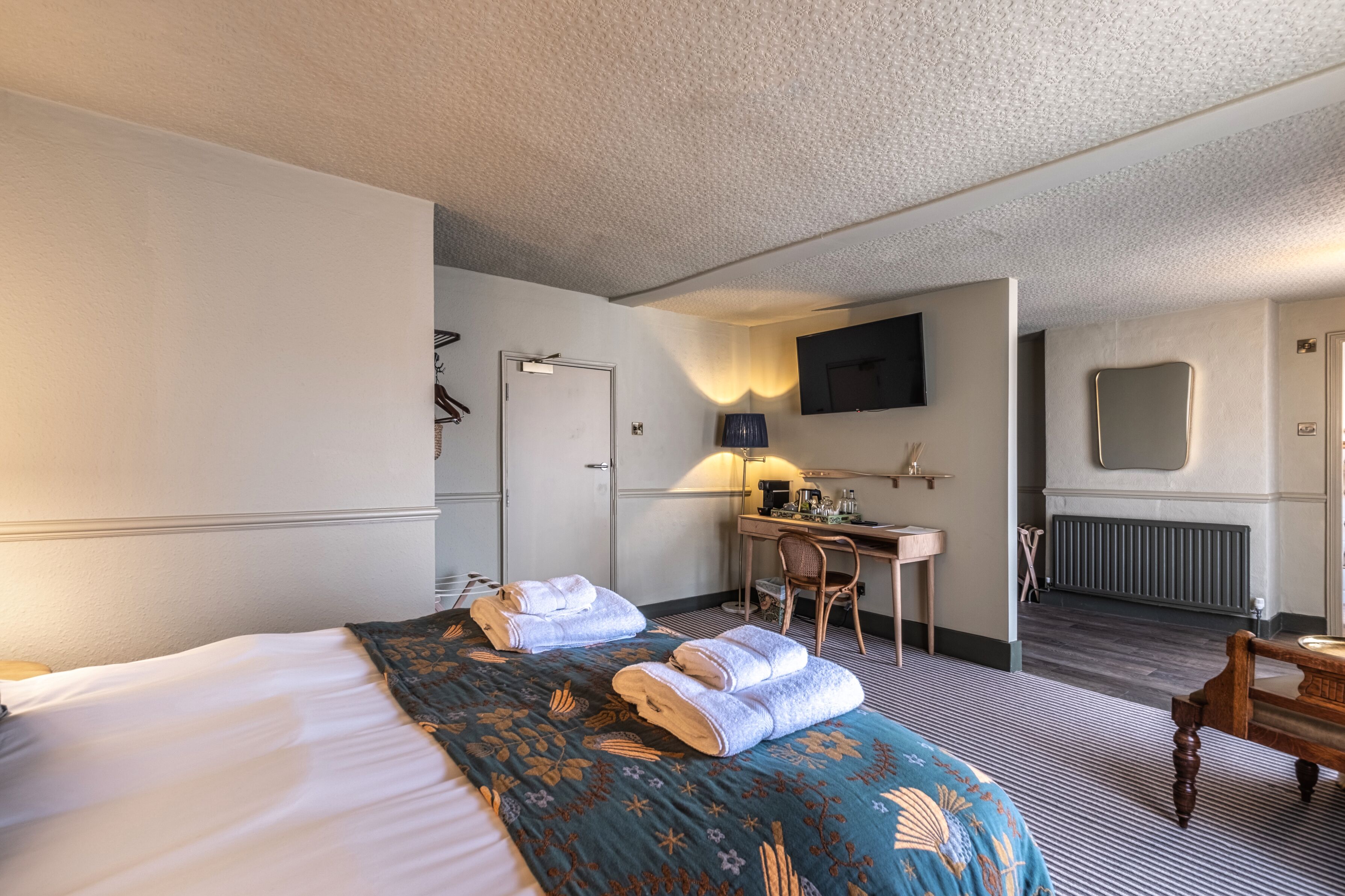 A hotel room with a bed, a desk, a chair, a television, and a mirror.