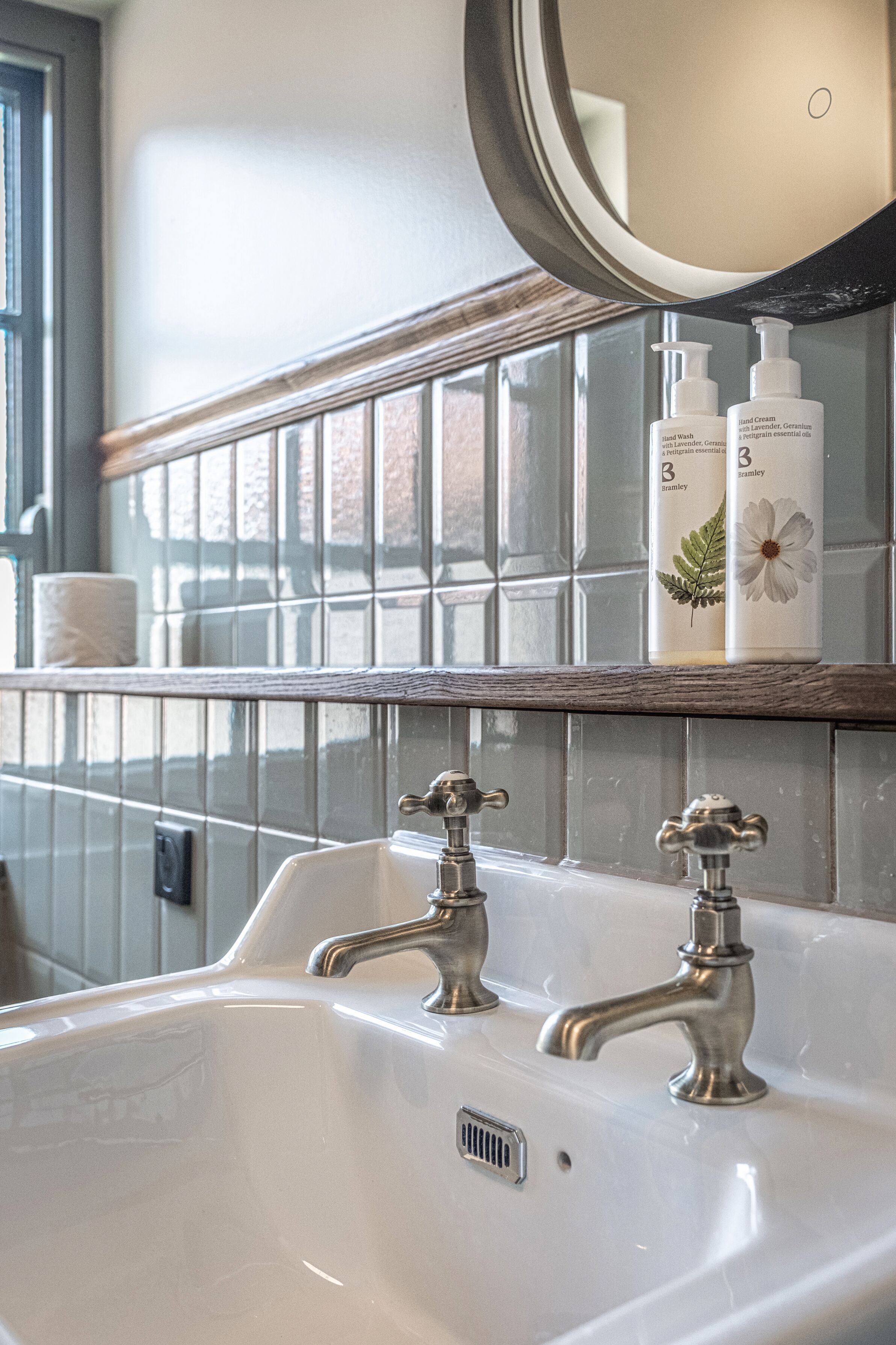 Une salle de bain avec un lavabo blanc, deux robinets et un miroir au-dessus. Deux flacons de crème pour les mains sont posés sur le mur.