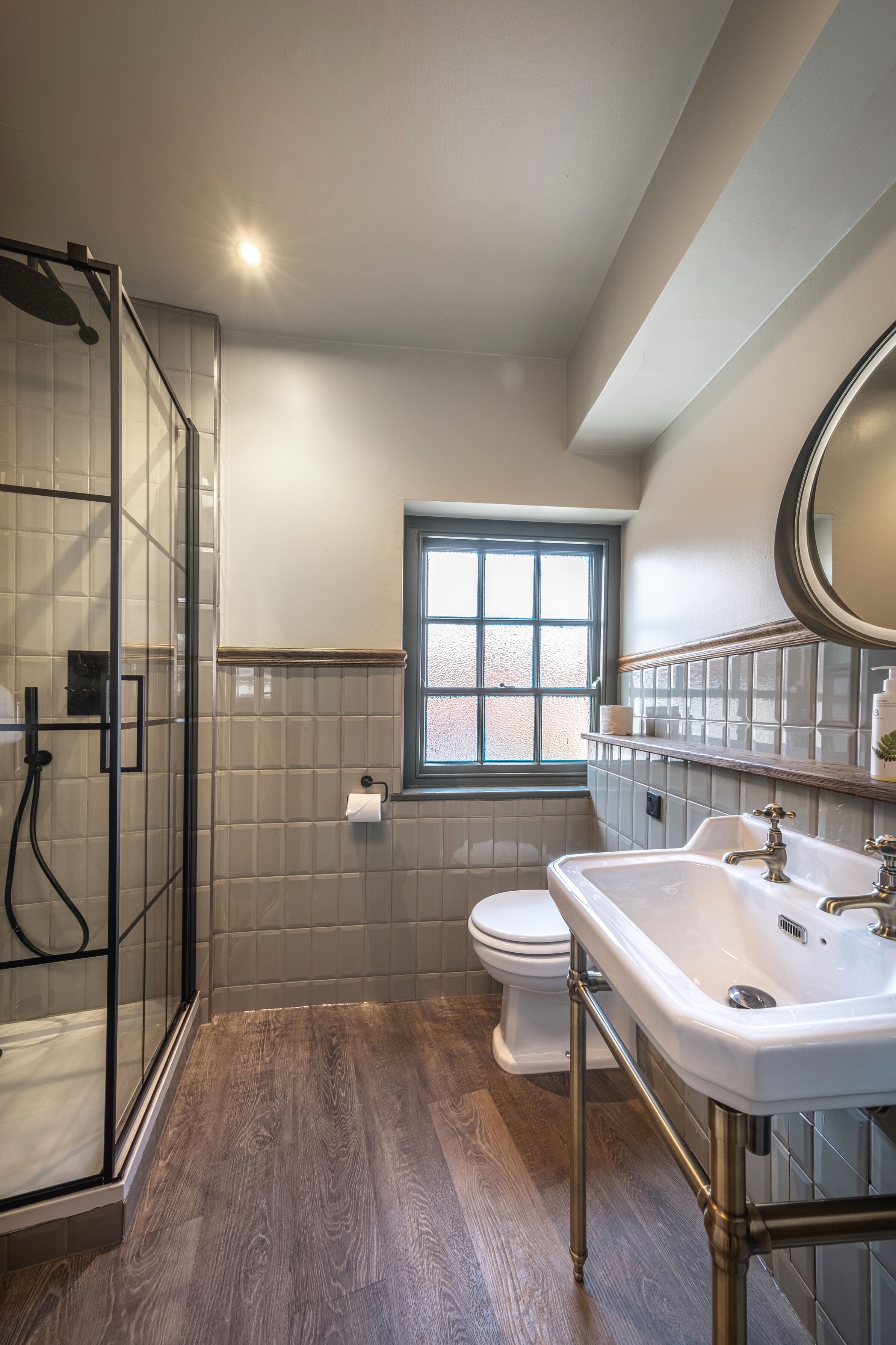 A bathroom with a glass shower enclosure, a toilet, a sink with a mirror, and a window.