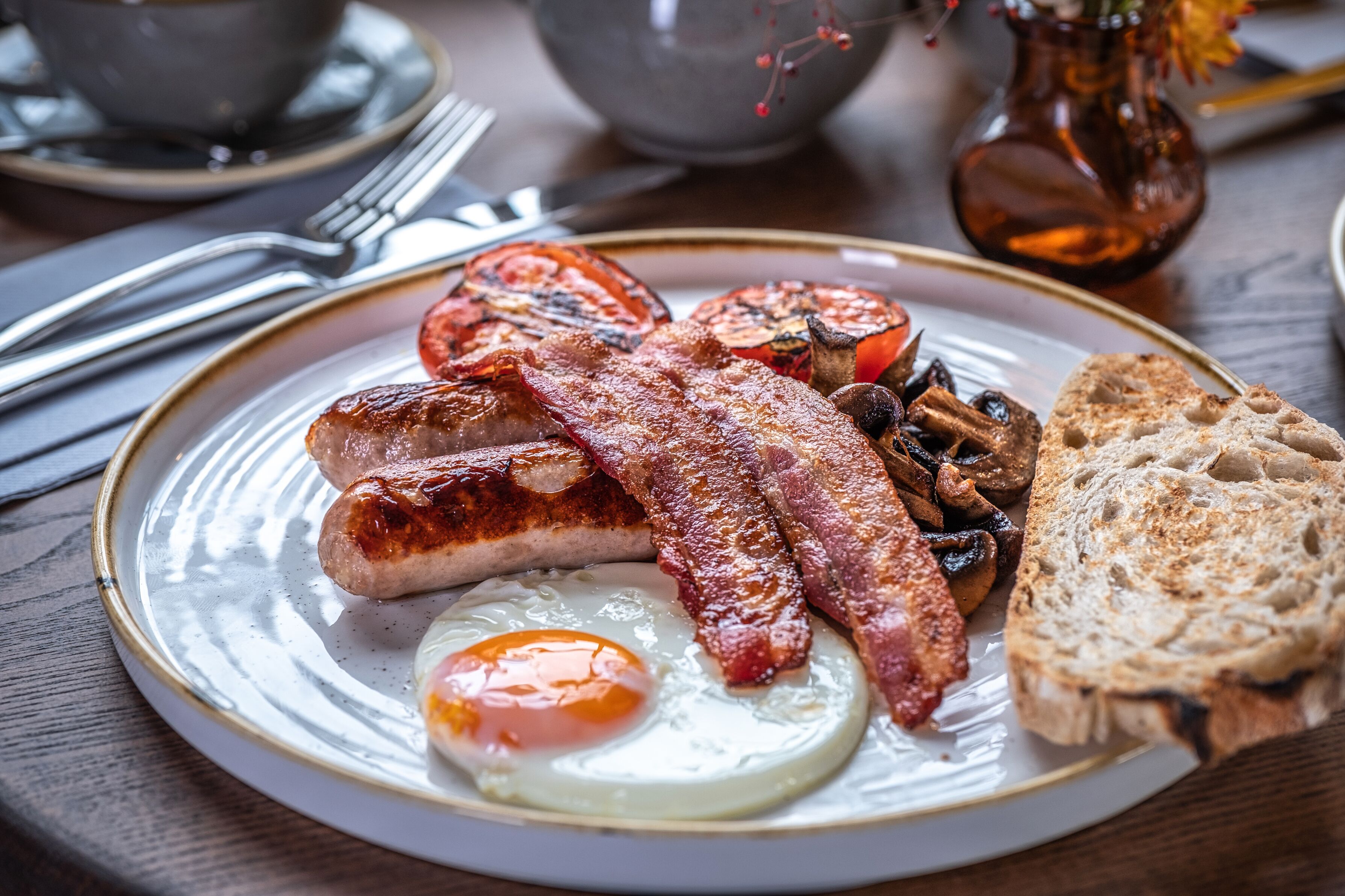 Un plato de desayuno con huevos, tocino, salchichas, champiñones y tostadas.