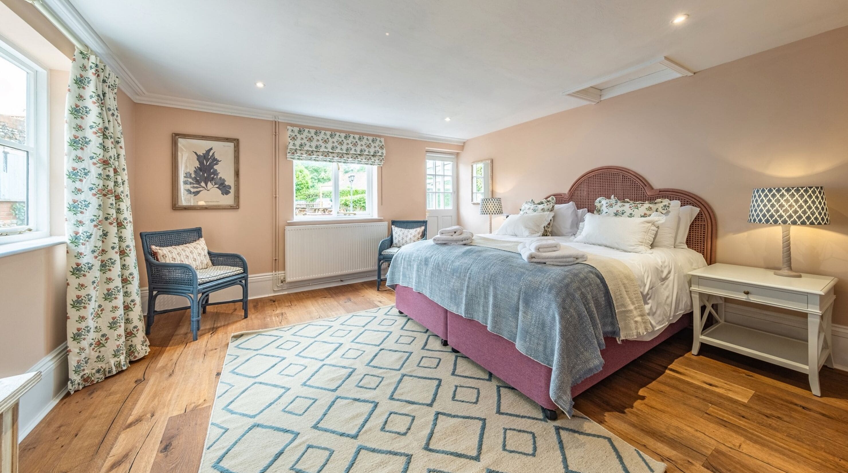 A bedroom with a bed, bedside tables, a chair, a window with curtains, and a radiator.