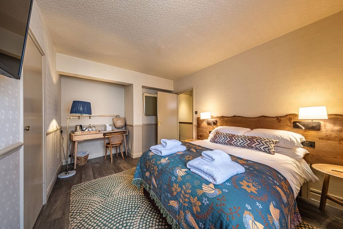 A hotel room with a bed, bedside table, lamp, desk, chair, and a small round table.