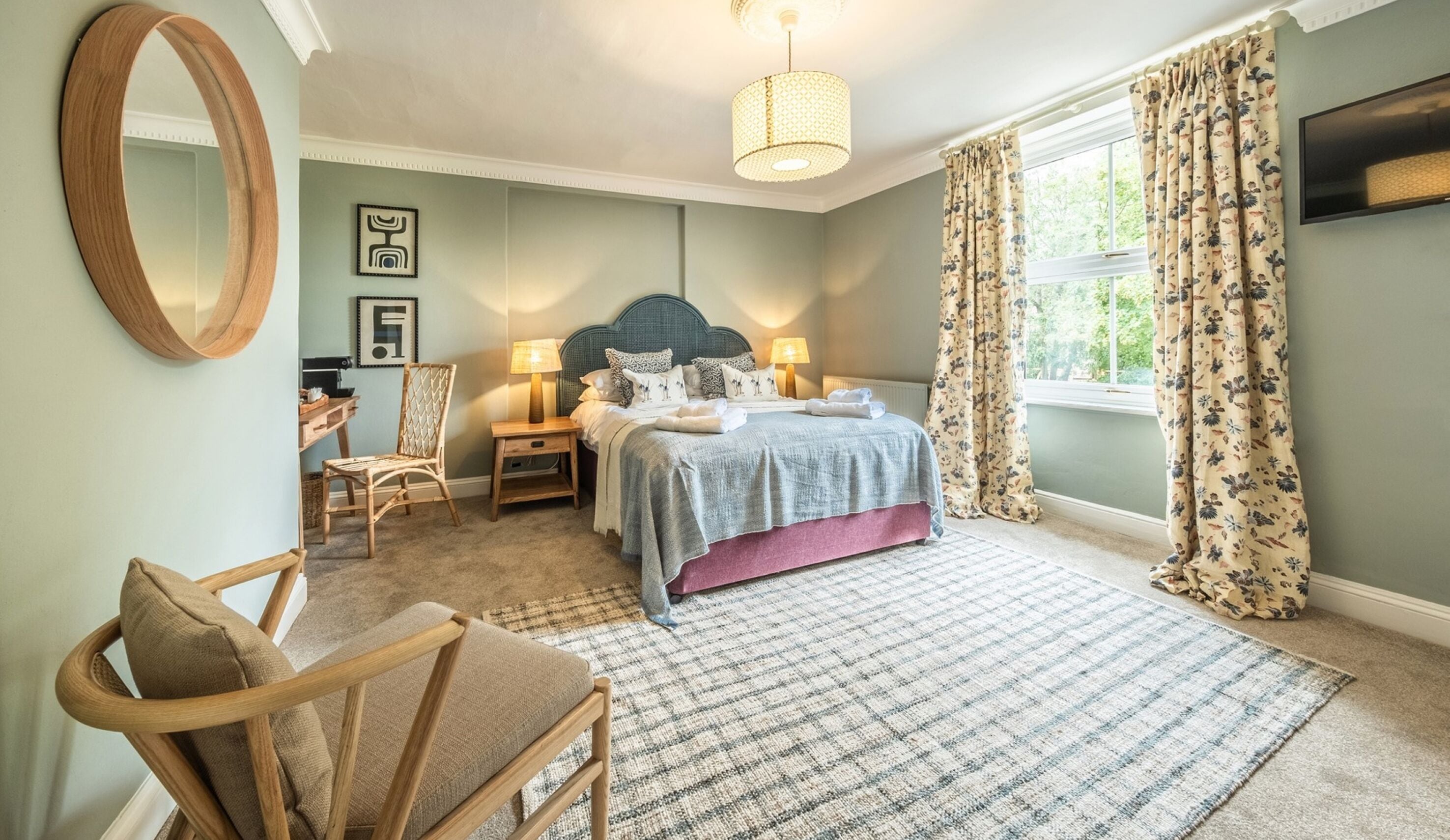 A bedroom with a bed, two bedside tables, a chair, a mirror, and a window with curtains.
