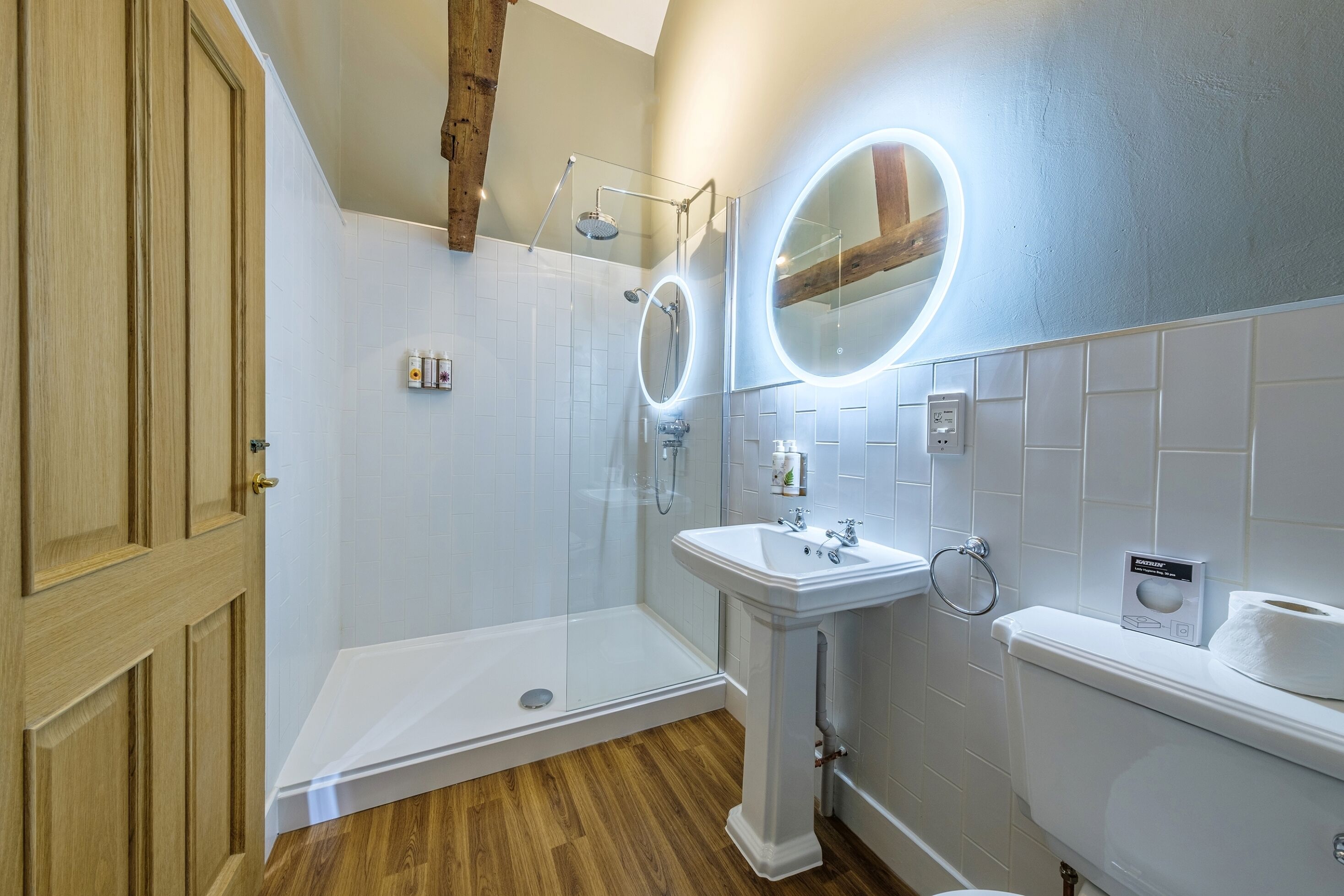 A bathroom with a shower, sink, toilet, and wooden door.