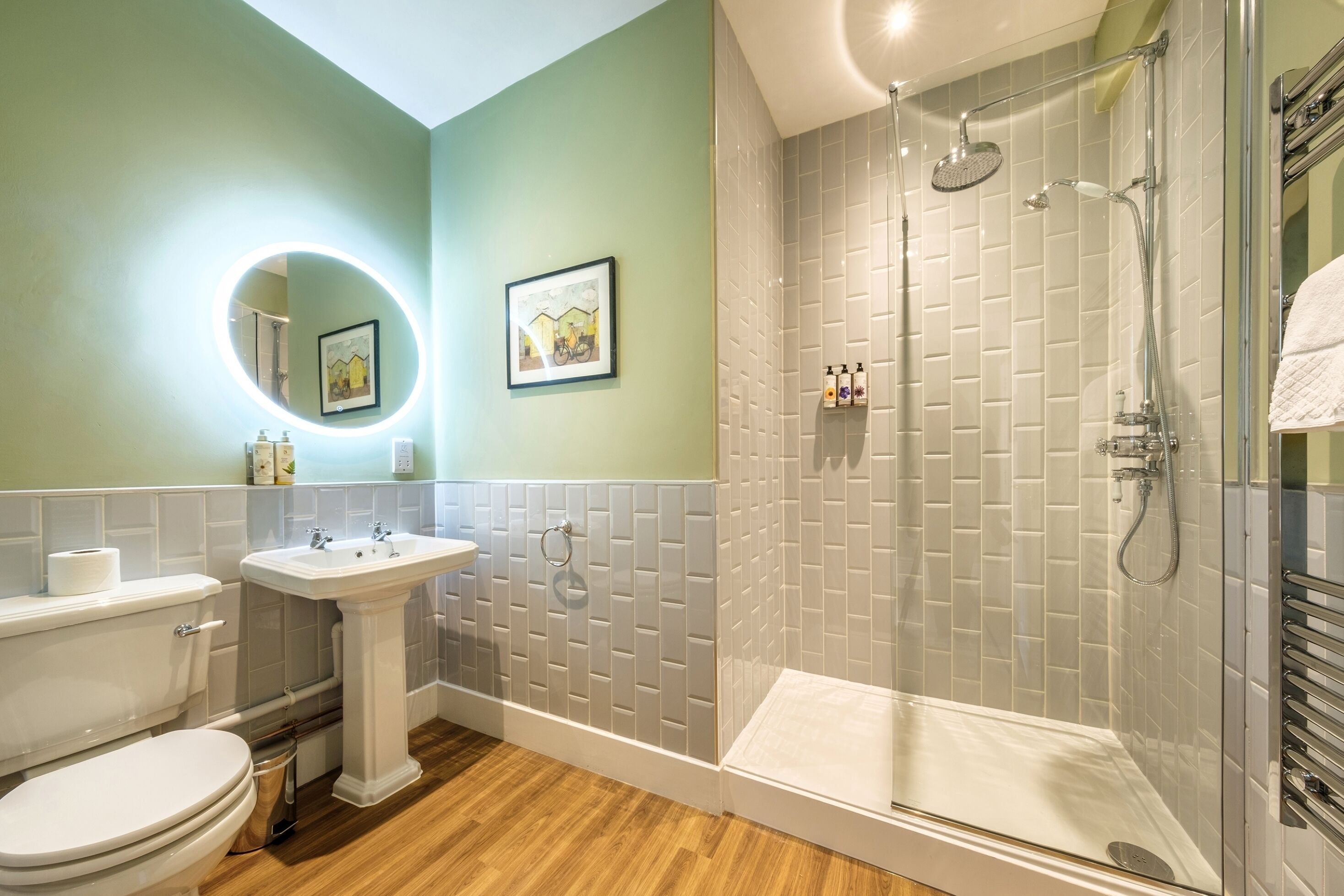 A bathroom with a toilet, pedestal sink, and a glass-enclosed shower area.