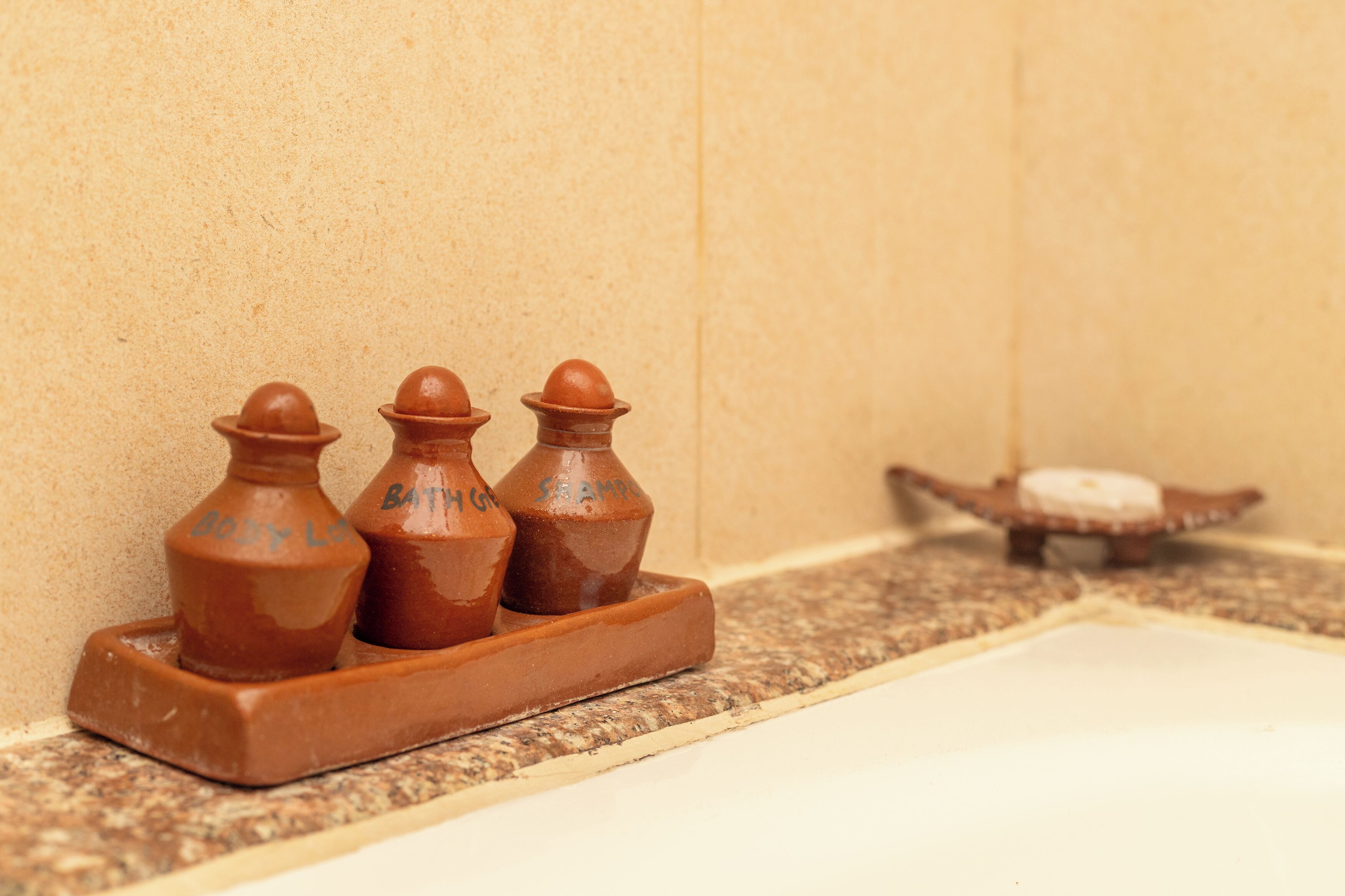 A bathroom with a brown ceramic soap dish and a small wooden soap dish on a granite countertop.