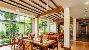 A dining area with wooden tables and chairs, large windows, and potted plants. - Atithi Resort & Spa (Pokhara)