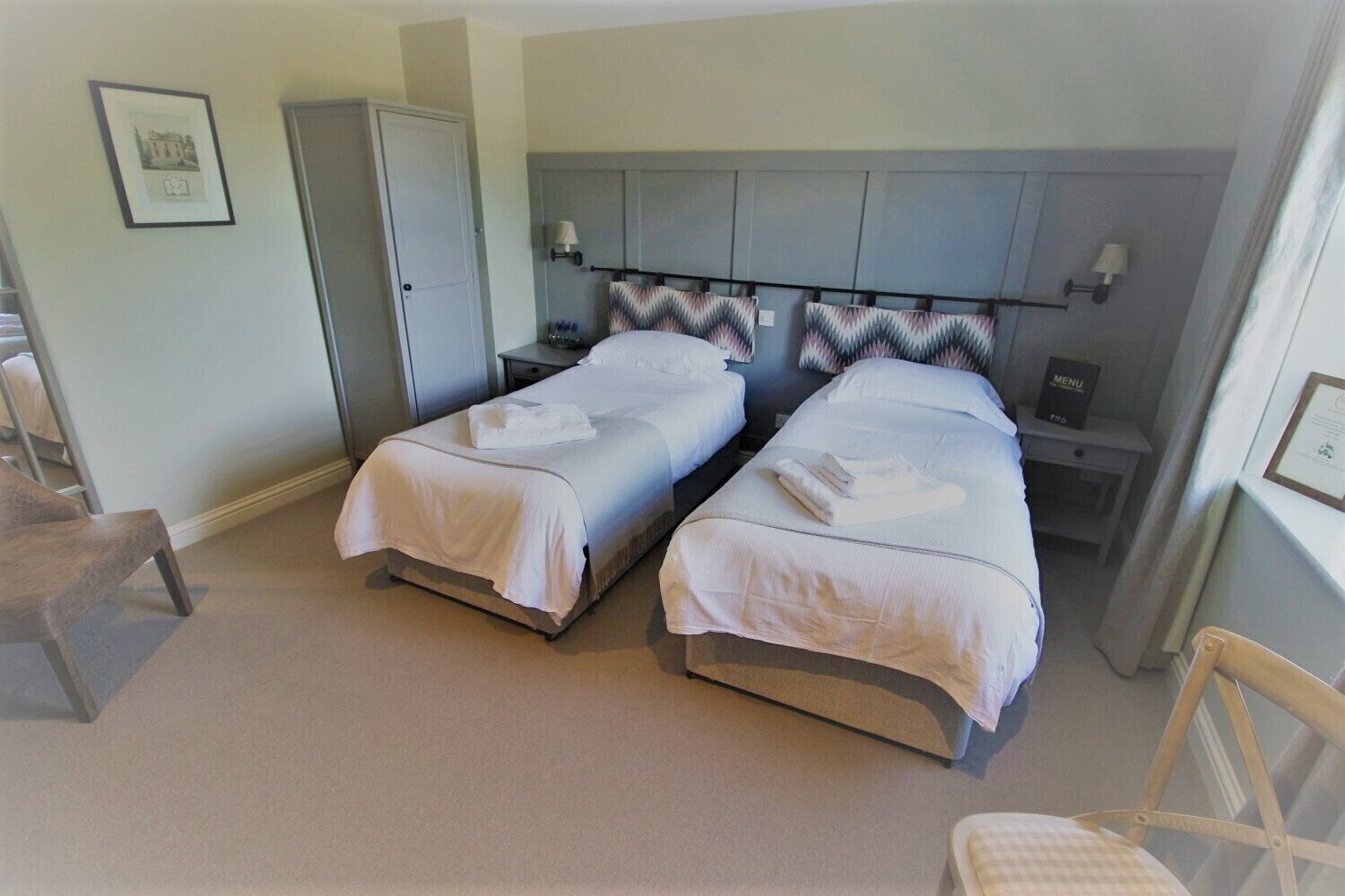 A twin room with two beds, a wardrobe, a nightstand, a chair, and a framed picture on the wall.