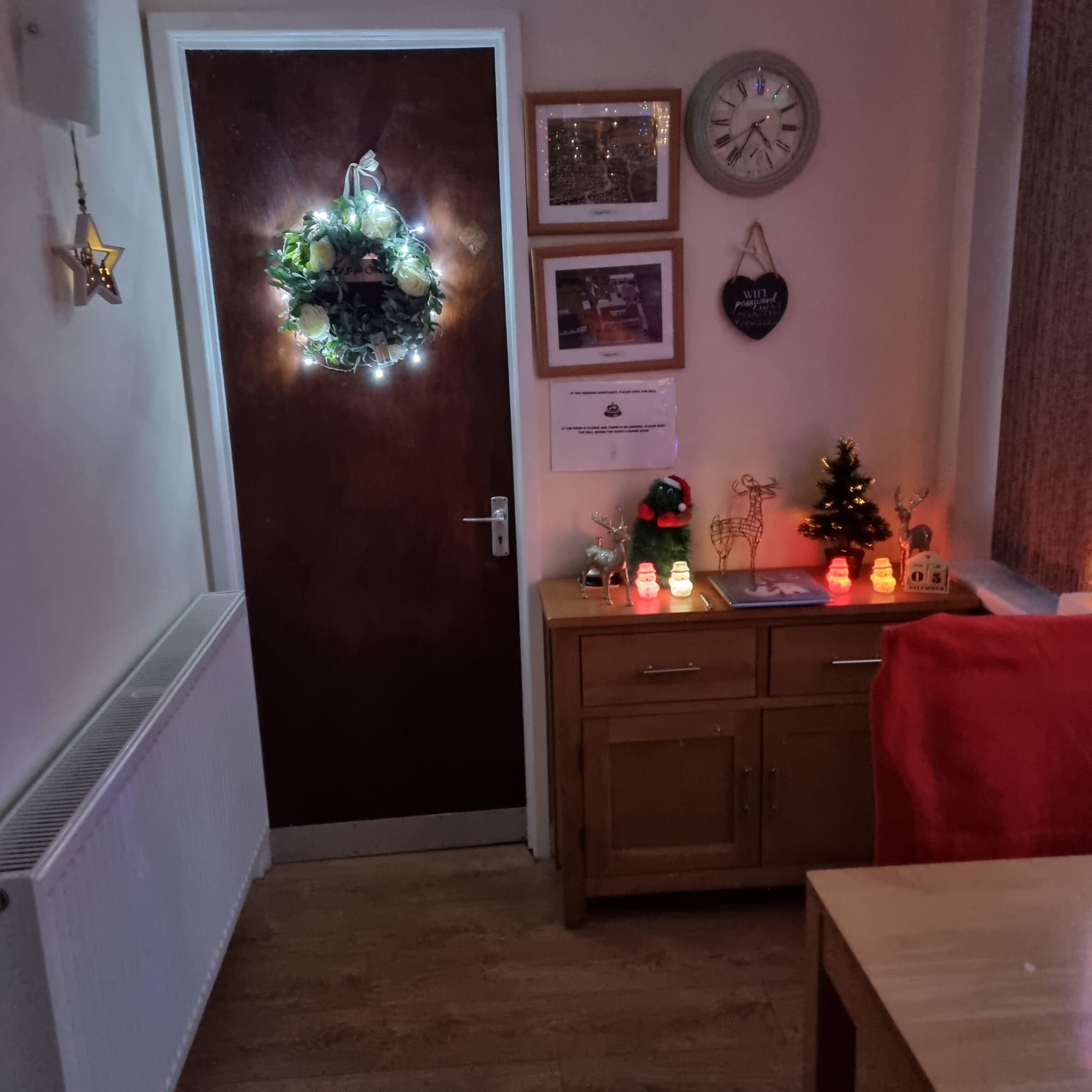 Una habitación con puerta de madera, una pequeña mesa, un armario y un reloj de pared.