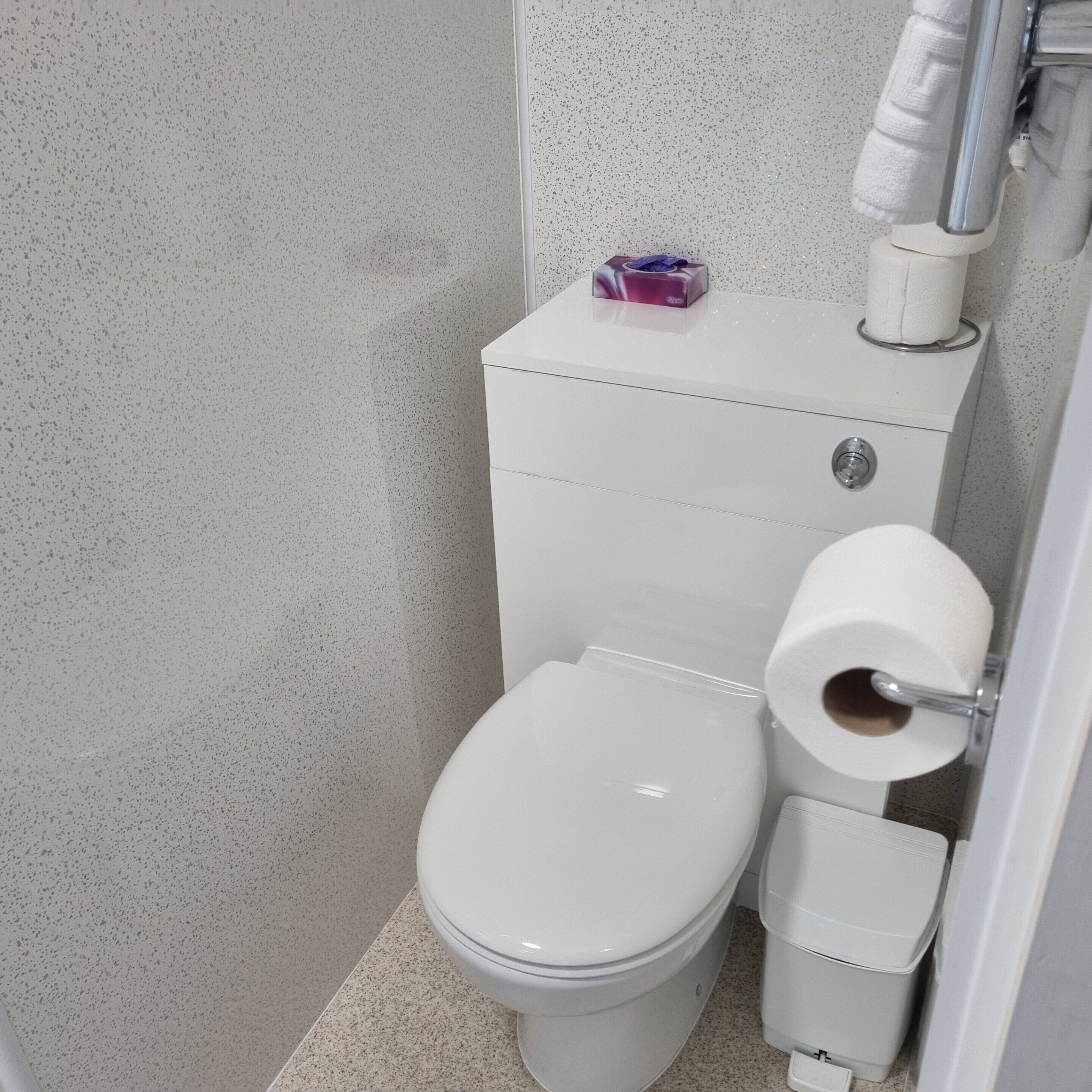 Ein kleines, weißes Badezimmer mit Toilette, einem Wäschekorb und einer Toilettenpapierhalterung.