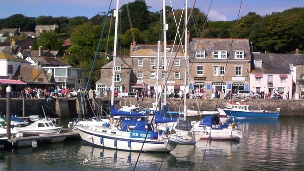 A harbor with boats docked, buildings in the background, and a crowd of people. - Trevarrian Lodge (Newquay)