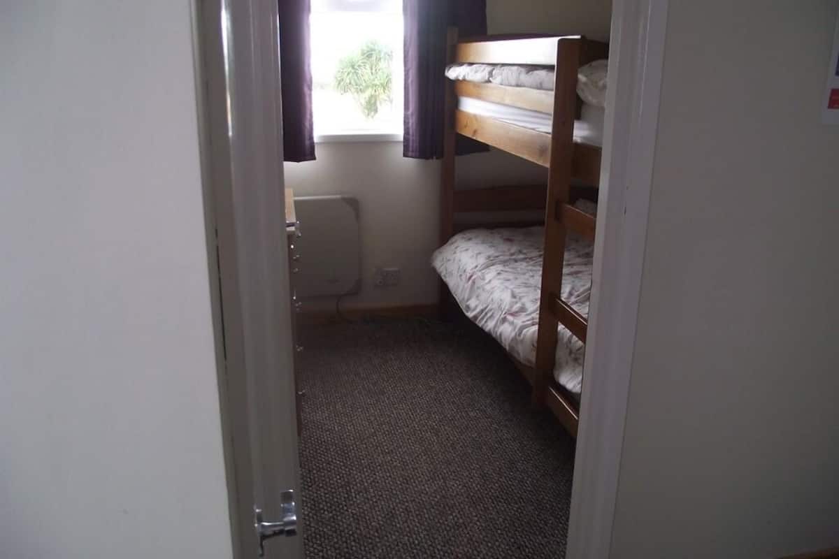 A small, dimly lit room with a bunk bed, a radiator, and a window with curtains.