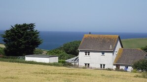 A coastal house with a sloped roof, a small attached shed, and a view of the sea. - Trevarrian Lodge (Newquay)