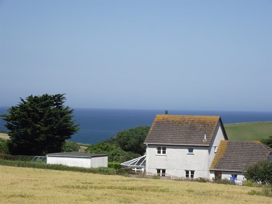 A coastal house with a sloped roof, a small attached shed, and a view of the sea.