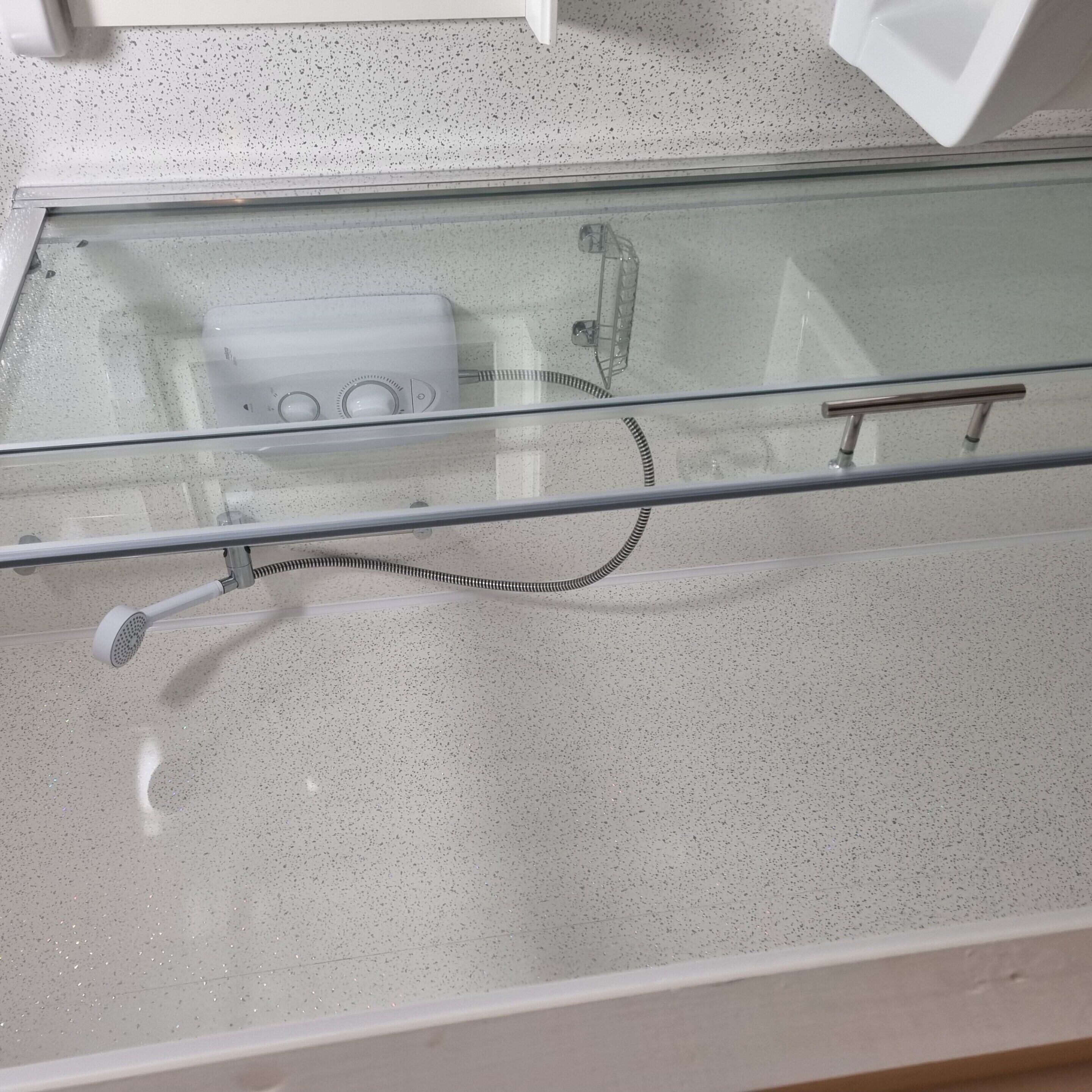 A bathroom with a glass shower enclosure, a handheld showerhead, and a control panel with knobs.