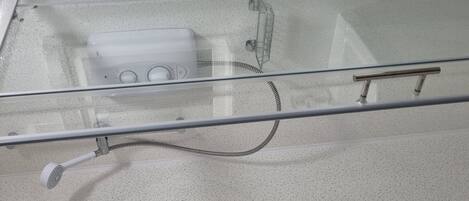 A bathroom with a glass shower enclosure, a handheld showerhead, and a control panel with knobs.