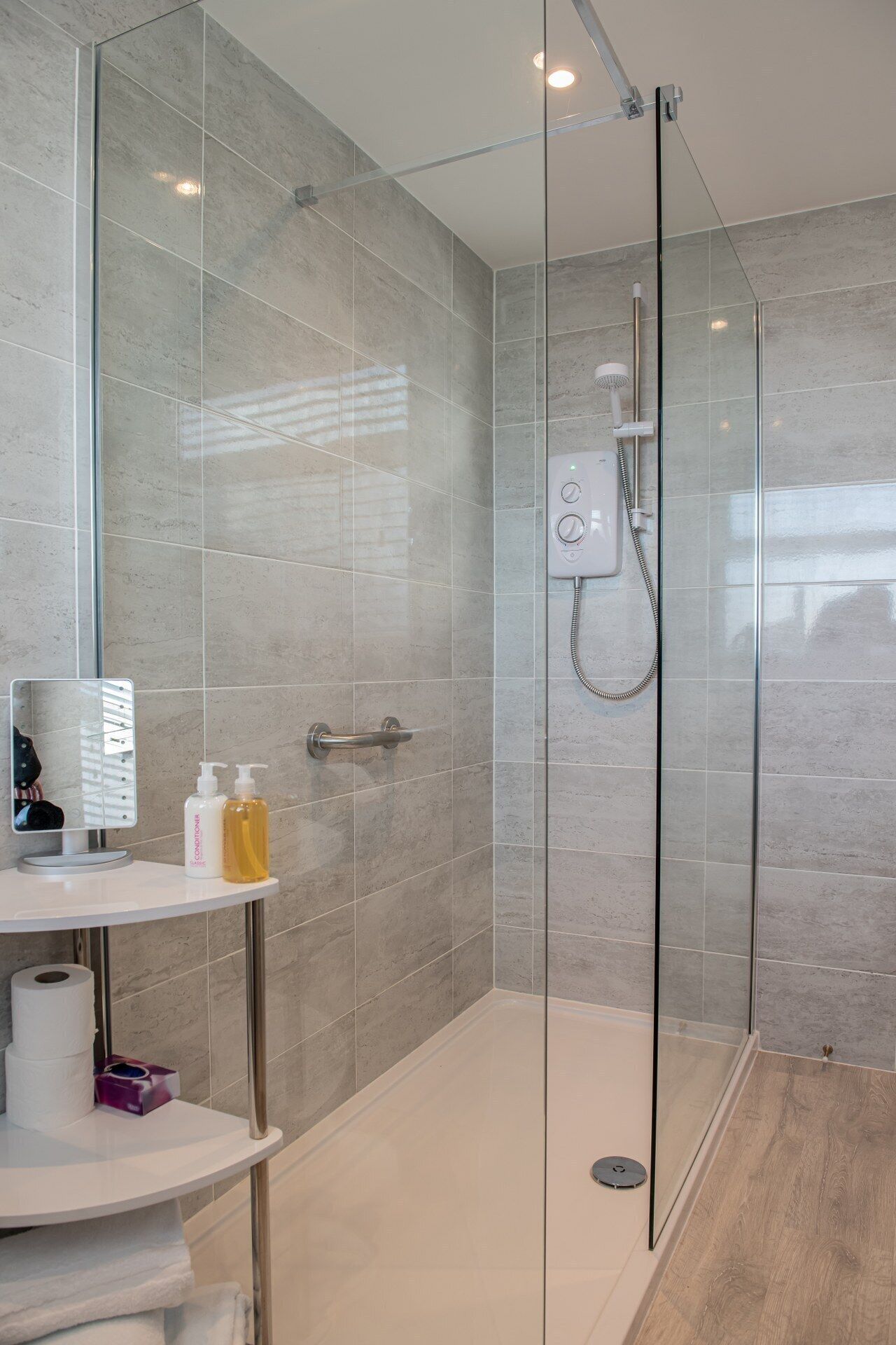 A modern bathroom with a glass-enclosed shower, a vanity with toiletries, and a mirror.