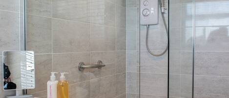 A modern bathroom with a glass-enclosed shower, a vanity with toiletries, and a mirror.