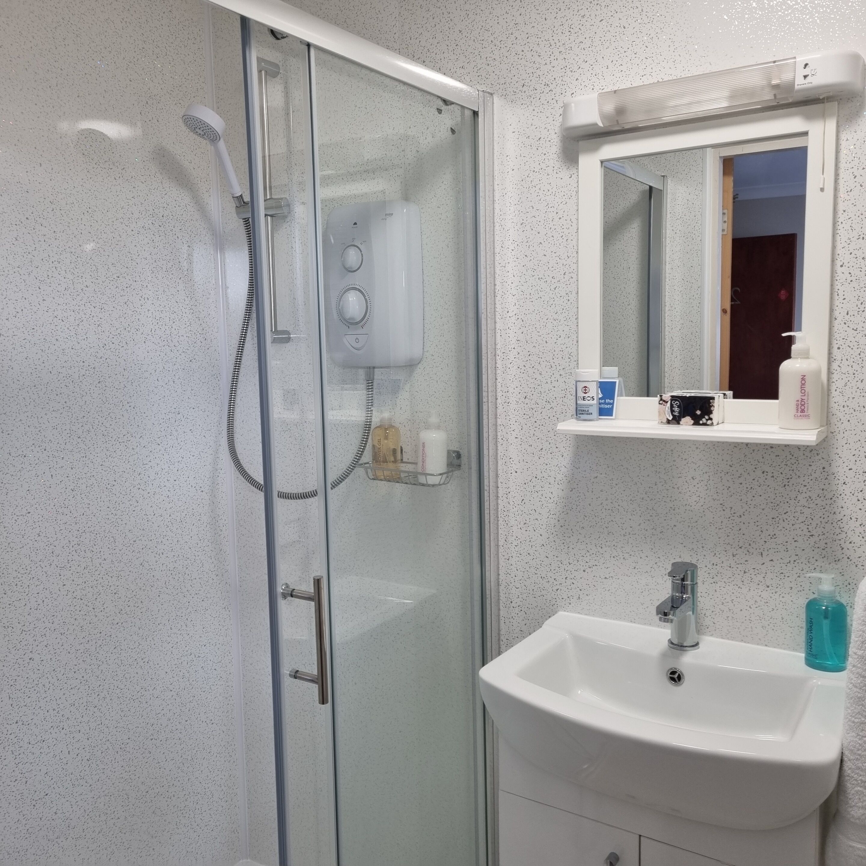 Une salle de bain avec une douche à parois de verre, un lavabo blanc et un miroir au-dessus.