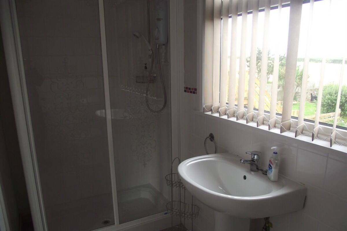 A bathroom with a glass-enclosed shower, a white sink, and a window with blinds.