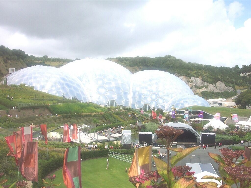 Una estructura grande y en forma de cúpula con un diseño hexagonal, rodeada por un área ajardinada con senderos y banderas.