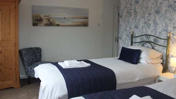 A bedroom with two beds, a wooden wardrobe, a chair, and a painting on the wall. - Waverley Bed & Breakfast (Minehead)