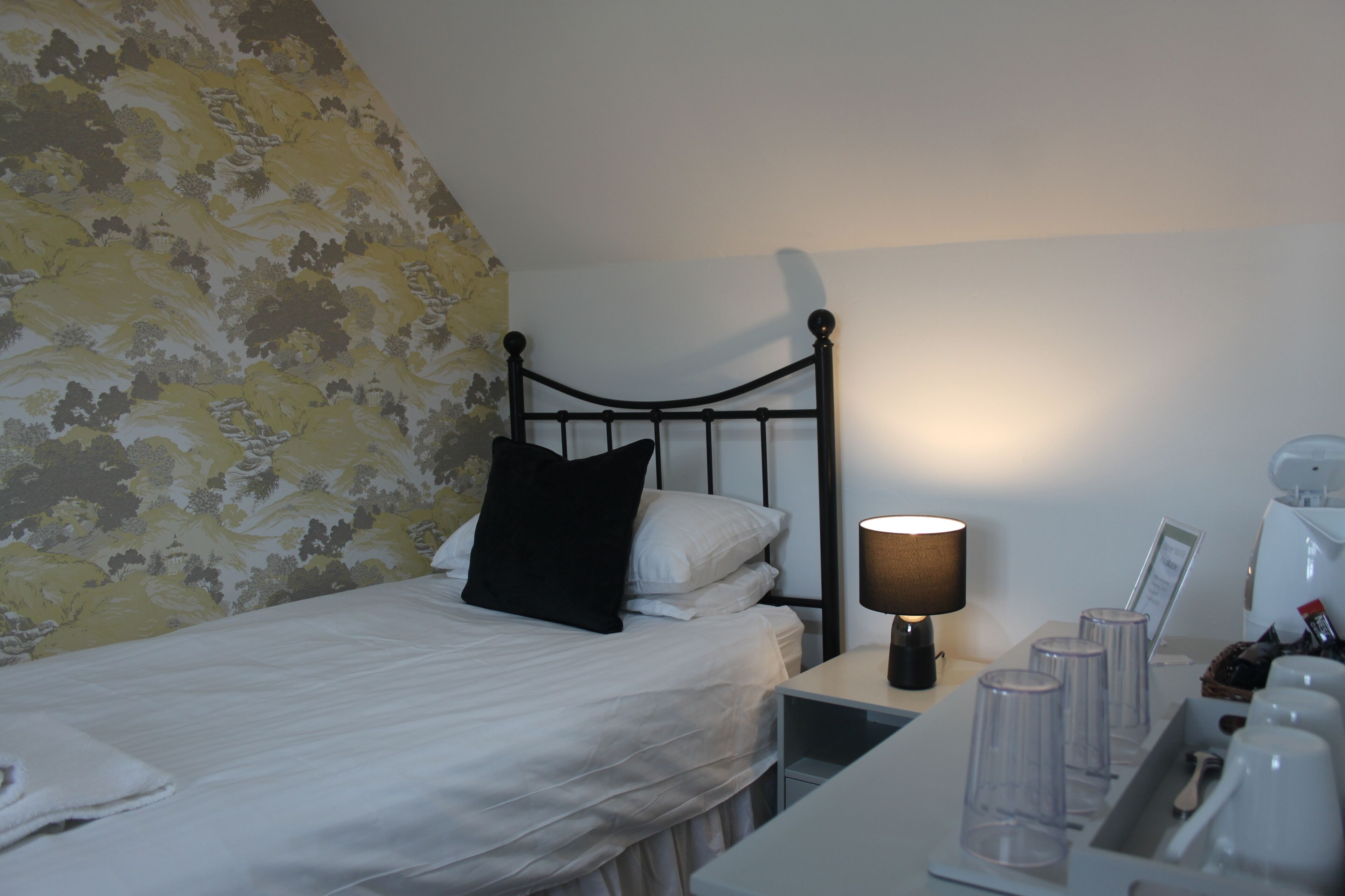 Une chambre d’hôtel avec un lit, une table de chevet, une lampe et un plateau avec des tasses et une cuillère.
