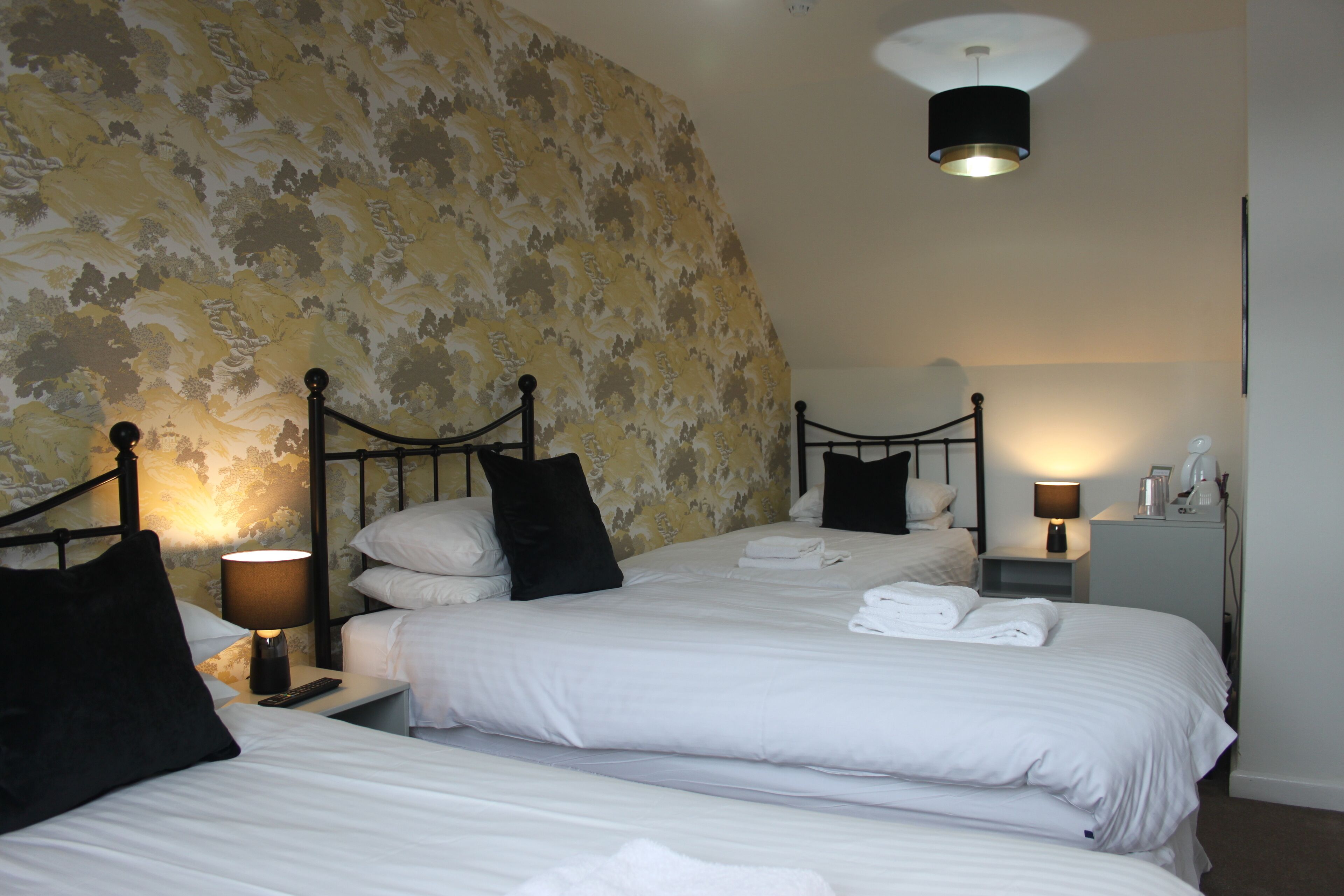 A hotel room with two beds, a large floral-patterned wall, and a ceiling light.