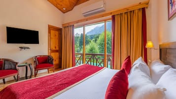 A hotel room with a large bed, a TV, a chair, and a balcony with a mountain view.