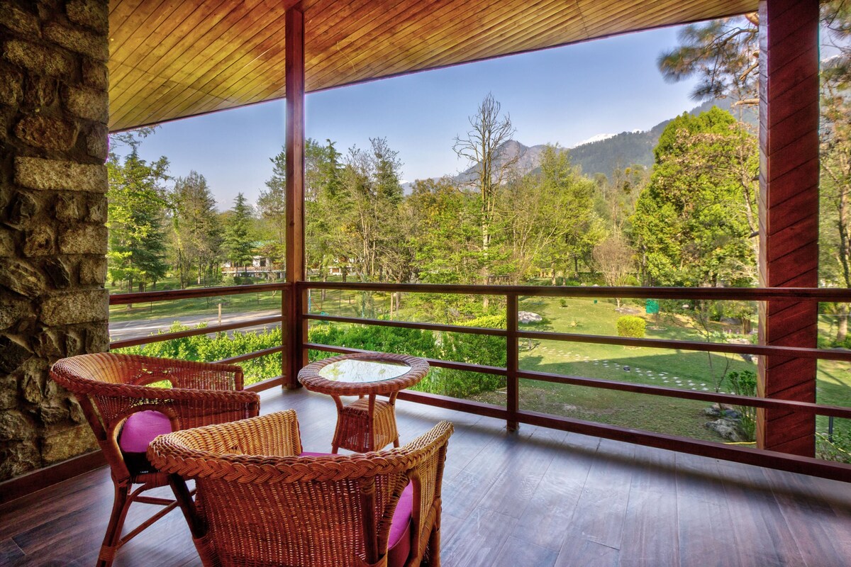 A balcony with wicker furniture and a view of a lush garden and mountains.