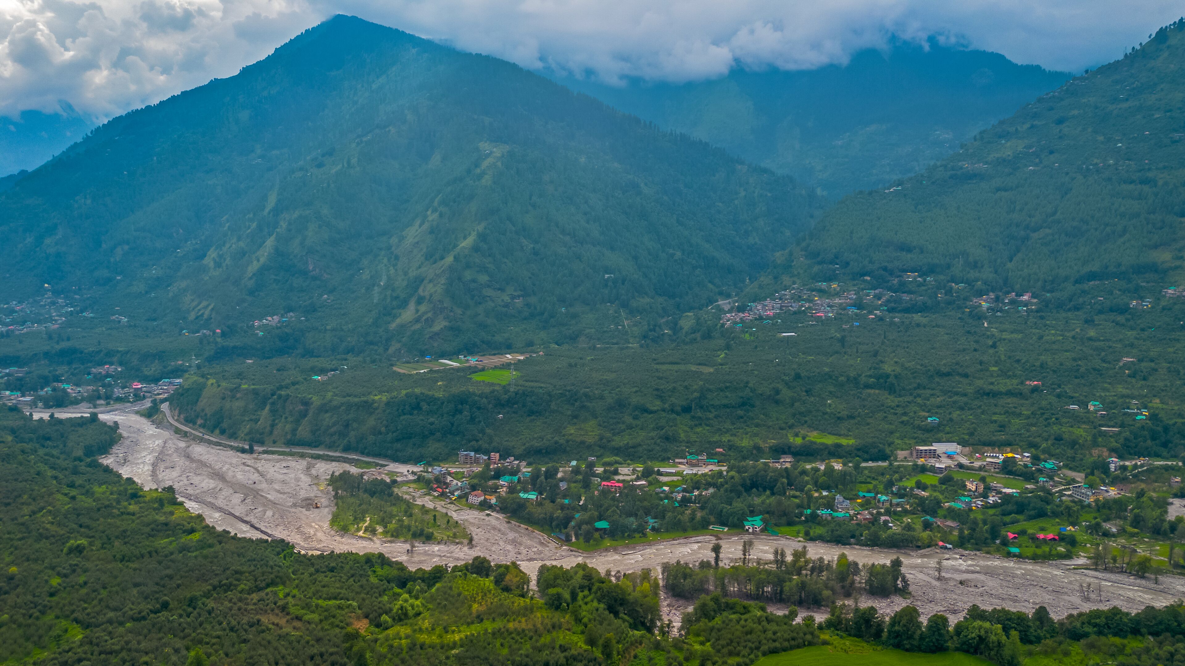A mountainous landscape with a river, a small settlement, and a prominent mountain peak.