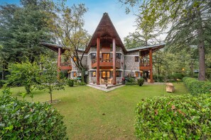 A large, multi-story building with a prominent triangular roof, surrounded by lush greenery and trees. - Span Resort & Spa, Manali - A Luxury Riverside Resort (Manali)