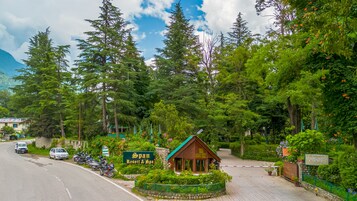 Entrada de un resort con un letrero, una pequeña construcción de madera y un camino pavimentado.