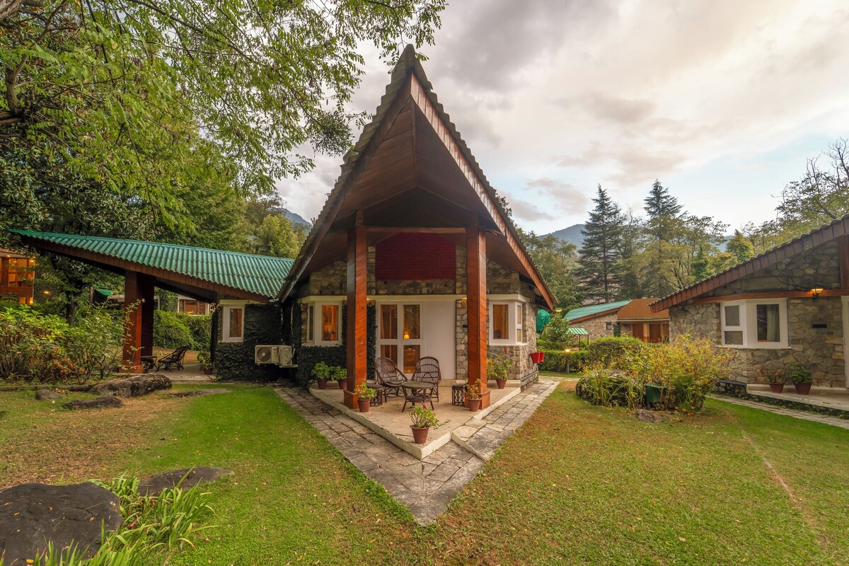 A traditional wooden house with a tiled roof, surrounded by lush greenery and a stone pathway leading to the entrance.