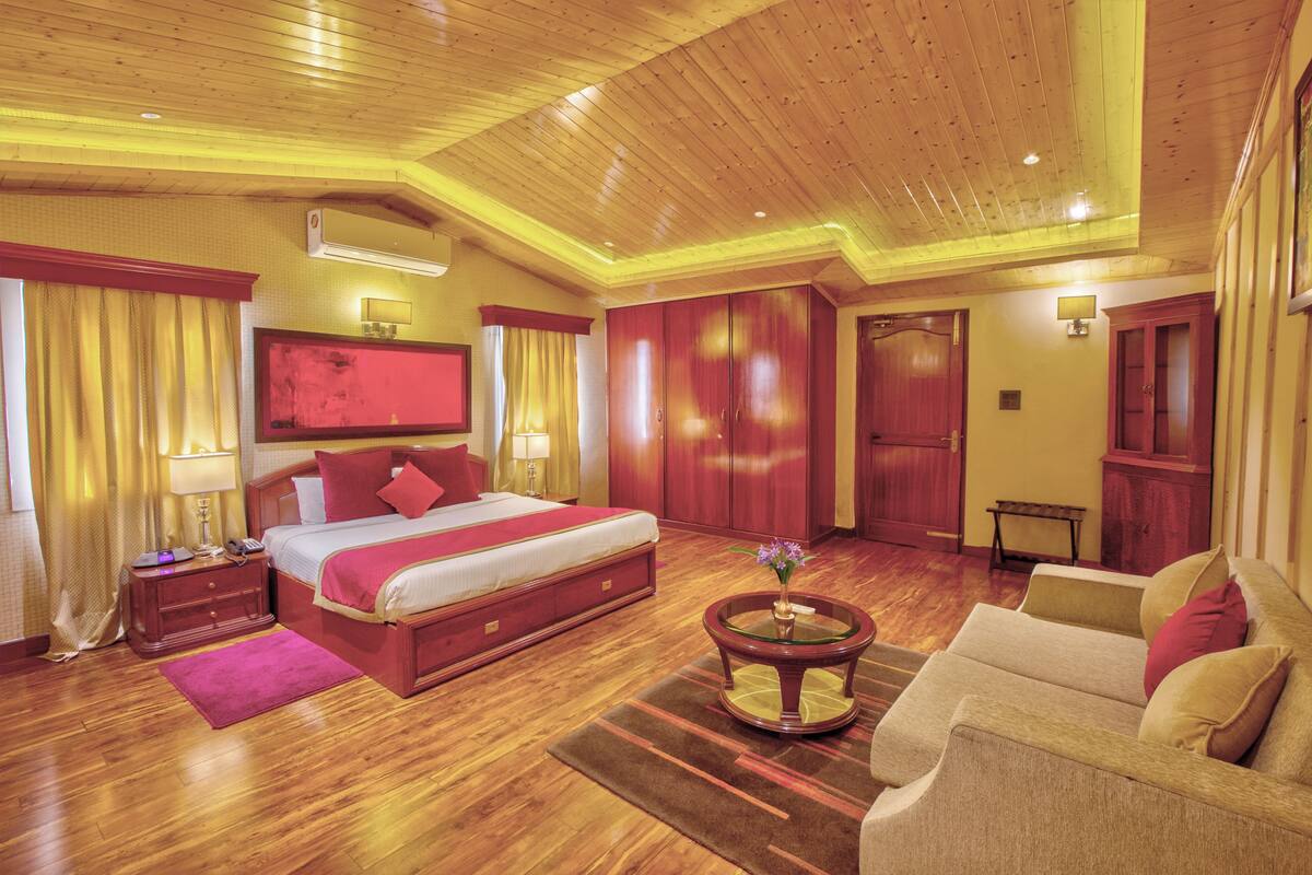 Une chambre d’hôtel spacieuse avec un grand lit, un coin salon comprenant un canapé, une table basse et un téléviseur fixé au mur.