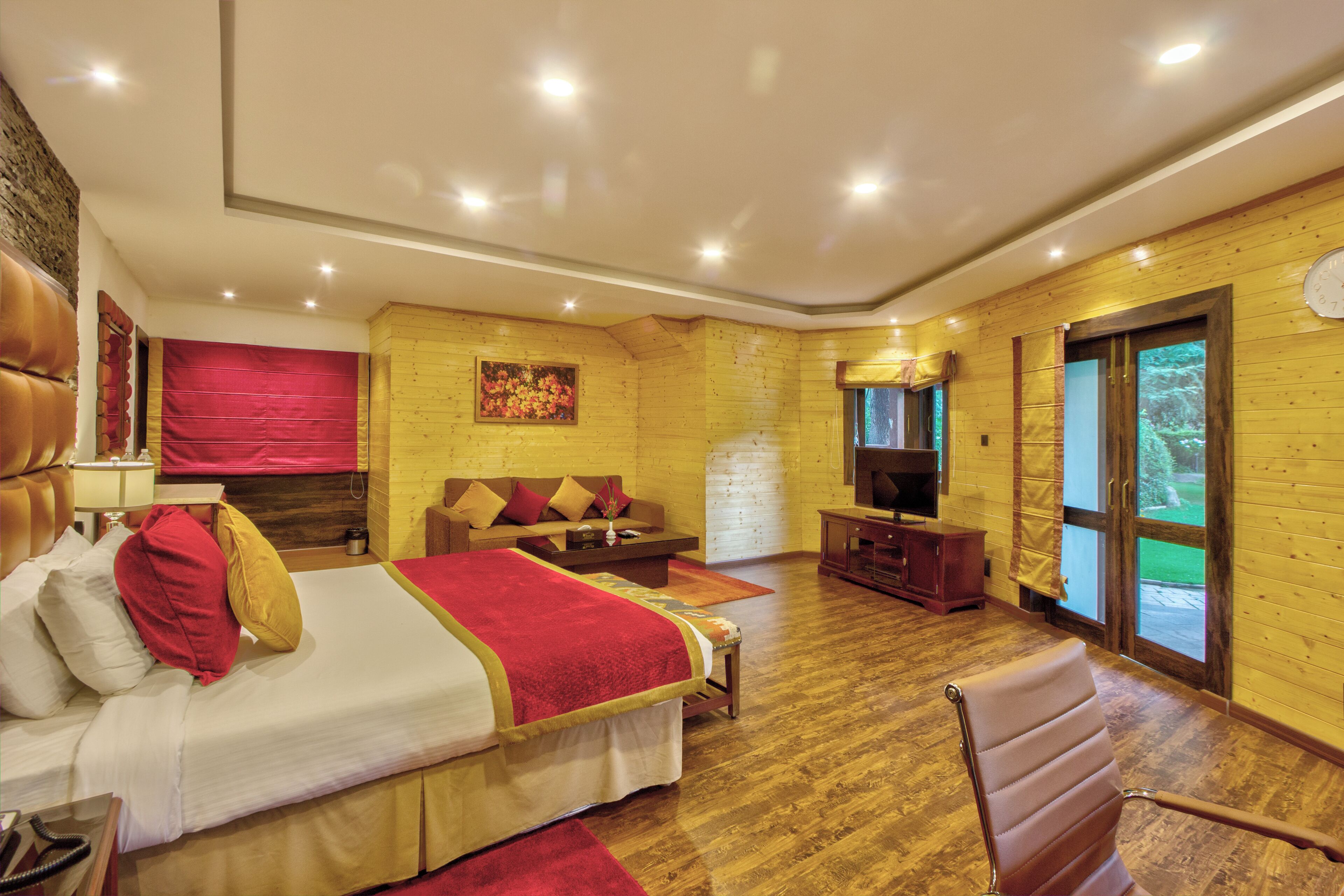 A spacious room with a large bed, a sofa, a TV, and a wooden floor.