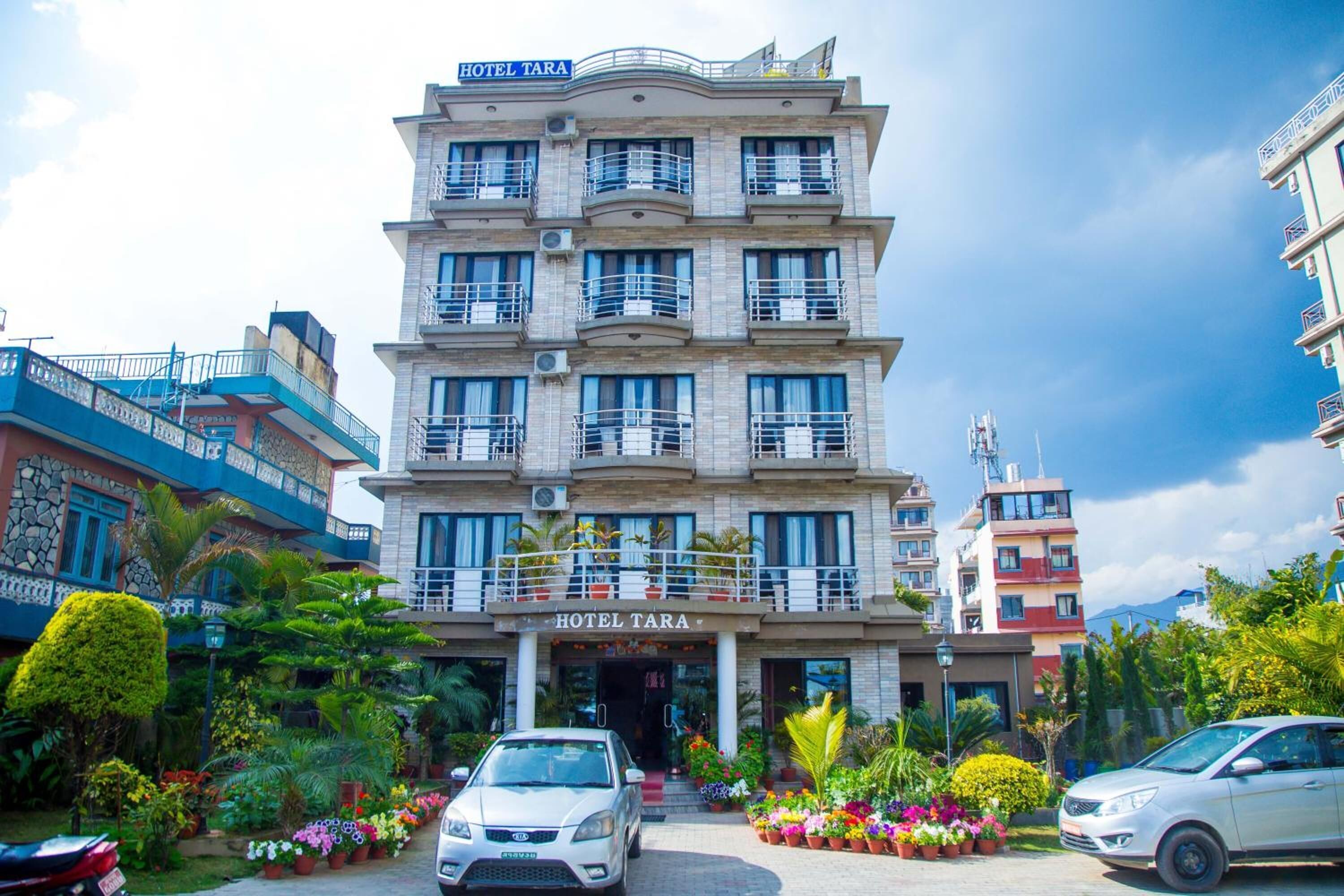 Ein mehrstöckiges Hotel mit Balkonen, einem Schild mit der Aufschrift "HOTEL TARA" und einem gepflegten Garten mit verschiedenen Pflanzen und Blumen.