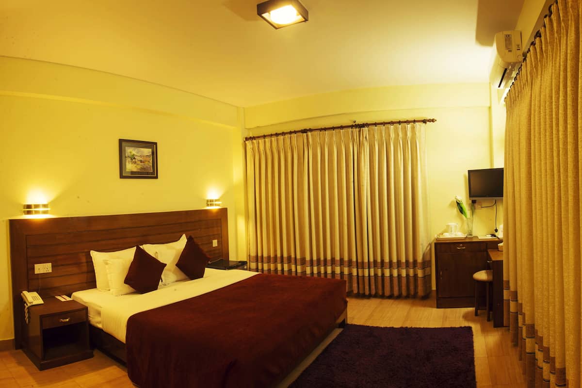 Une chambre d’hôtel comprenant un lit, des tables de chevet, un bureau avec une chaise, une télévision et des rideaux.
