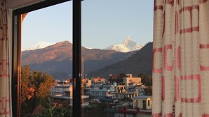 A view through a window with a curtain, featuring a mountainous landscape with snow-capped peaks in the background and a town with buildings in the foreground. - Hotel Tara (Pokhara)