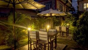 An outdoor patio with tables and chairs, surrounded by plants and a building with a stone facade. - Hotel Tara (Pokhara)
