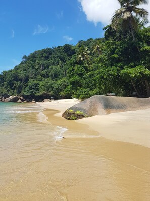 A beach with clear turquoise water, sandy shore, and lush green vegetation. - Cabanas Paraíso (Angra dos Reis)