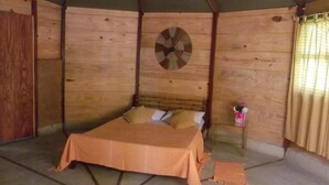 A tent-style room with a bed, a circular wall decoration, and a small table with a pink item. - Cabanas Paraíso (Angra dos Reis)