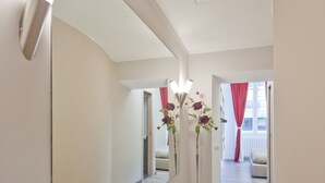 A hotel hallway with a large mirror, a vase with flowers, and a light fixture. - Relais Sistina (Rome)